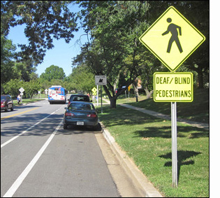 Two photographs show a two-lane street with a bike lane and a parking lane on the right, a shoulder on the left.  A post on the right has two signs -- on top is a yellow diamond-shaped sign showing a sillouette of a pedestrian walking, and below that is a rectangular sign saying 'DEAF-BLIND PEDESTRIANS.'  About 150 ahead of that we can see another yellow sign at a crosswalk.